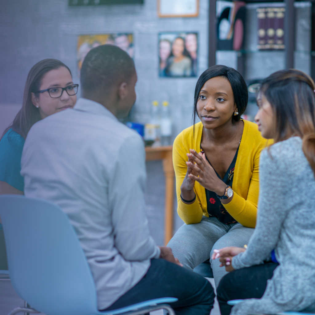 diverse group of five individuals discussing and listening in a circle with black woman facilitating